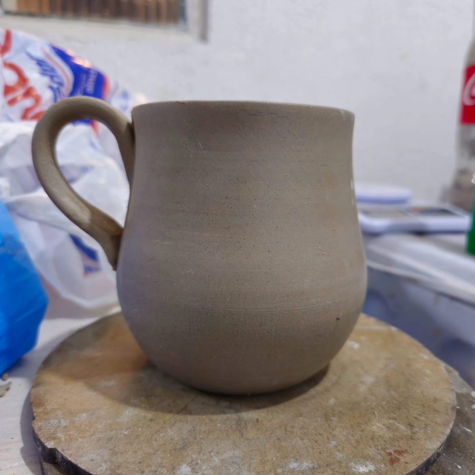 Verso de uma caneca de argila crua com perfil suavemente curvo.